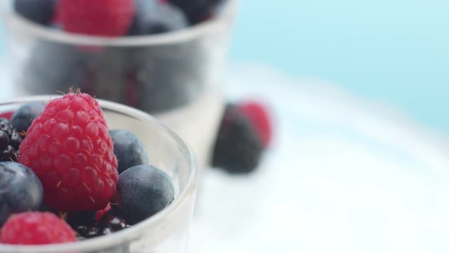 glasses full of yogurt and berries on a crystal plate turning on it's axis in studio minimalist clip
