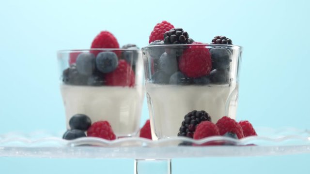 woman hand serve putting on a crystal plate the second one glass with greek yogurt with berries