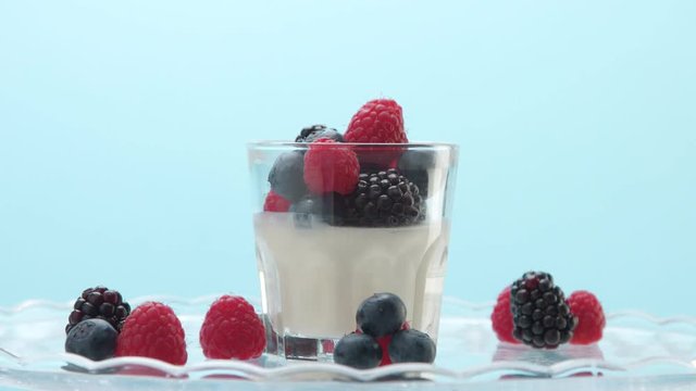 creamy vanilla mouse dessert or panna cotta or greek yogurt with berries on plate decorated with raspberry blueberry, blackberry on light blue background. Minimalism food clip