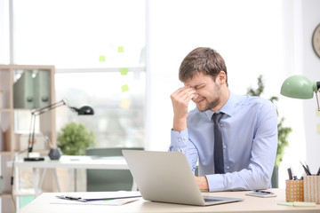 Fototapeta premium Young man suffering from headache in office