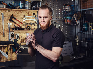 Handsome stylish redhead worker, cleaning his dirty hands after repairing working in a workshop. 
