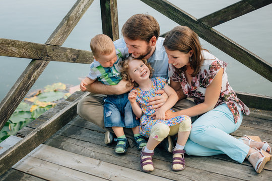 Happy smiling Family Sitting On Wooden Jetty having fun and playing. Parents with cute kids outdoors