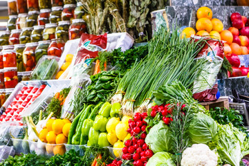 A lot of different vegetables and fruits are on the shelves in the market.