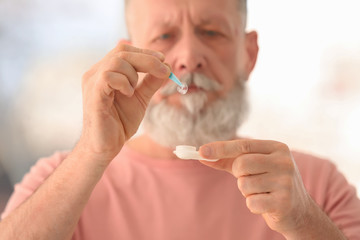Fototapeta premium Senior man taking contact lens from container on blurred background