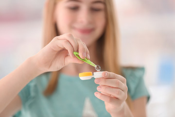 Teenage girl taking contact lens from container on blurred background