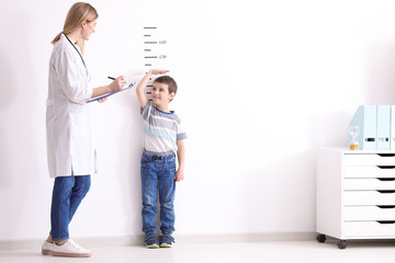 Female doctor measuring height of little boy in clinic - obrazy, fototapety, plakaty