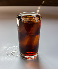 Cola with ice in glass on white table