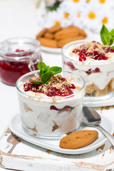 dessert in a glass with biscuits, cream and jam, vertical closeup