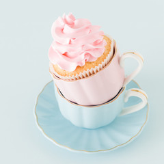 Cupcake with gentle pink cream decoration in two cups on blue pastel background.