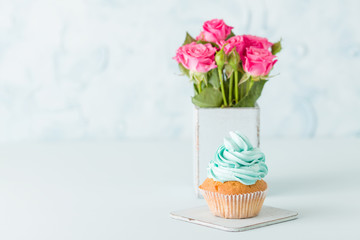 Cupcake with gentle blue cream and pink roses in retro shabby chic vase on blue pastel background.