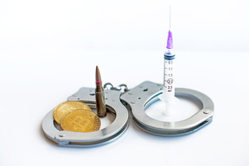 Bitcoins, a bullet, a syringe and handcuffs as an abstract symbol of crimes that can hide the cryptic currency