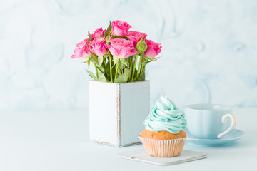 Cupcake with gentle blue cream and pink roses in retro shabby chic vase on blue pastel background.