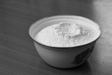 White enamel bowl with wheat flour on an old scratched table