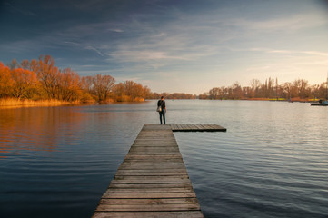 Blonde girl on a wooden landing stage overlooking a lake at sunset in Braunschweig, Germany