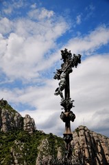 Obraz premium Cross with crucifixion of Jesus Christ on a mountain trail near Montserrat Monastery. The Montserrat mountain with strange weathered rocks. Catalonia, Spain.