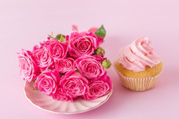 Cupcake with pink cream decoration and roses on pink pastel background.