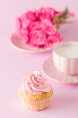 Cupcake with pink cream decoration and roses on pink pastel background.