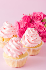 Cupcake with pink cream decoration and roses on pink pastel background.