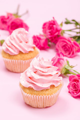 Cupcake with pink cream decoration and roses on pink pastel background.