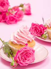 Cupcake with pink cream decoration and roses on pink pastel background.