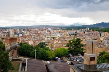 View of the city of Girona from the medieval pedestrian border wall. Roofs of houses, trees. Storm clouds over the city, somewhere sunlight makes its way through the clouds. Girona, Spain