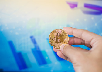 Close up man hand holding  bitcoin on a laptop with finance graph