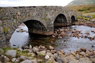 Fototapeta na wymiar Old massive stone bridge crossing shallow river in Sligachan, Isle of Skye, Scotland.
