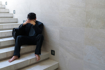 Concept of business failure : Young businessmen sit on the stairs and his hands clasped his head Because he is so desperate , stressed , sadness after knowing the bad news that he is unemployed.