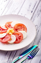 A beautiful spring salad from tomatoes, onions, cheese and green dressing. Eating on a large elegant plate. Unusual iridescent cutlery. Delicious and easy food for a healthy diet from a nutritionist.