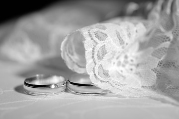 Wedding rings on white fabric framed with tulle with lace. Close-up. Black and white.