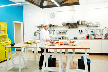 Cooking specialist in uniform chopping fresh ingredients for salad while preparing food for clients of restaurant