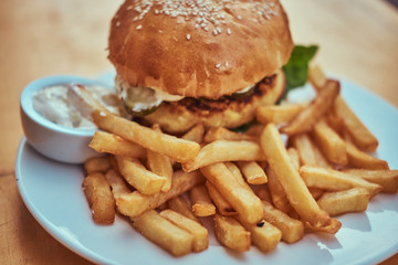 Close-up image of a hamburger with French fries and spicy sauce on a white plate. Unhealthy food concept