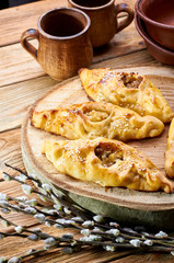 Traditional Russian, Ukrainian, Belarusian, Slavic pies with hole in center. Rasstegay - pastry with cabbage, meat, fish, mushrooms. Rustic pottery in the background. Branch of a blossoming willow.