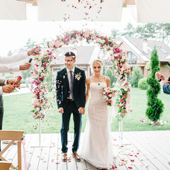 The bride and groom go through the arch, theirs sprinkled with leaves of roses and colored...