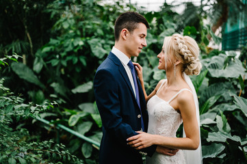 The bride looks at the groom. The groom in wedding suit and the bride in dress are standing and...