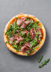 Prosciutto arugula homemade pizza  on grey background, top view. Delicious appetizers in mediterranean style. Copy space