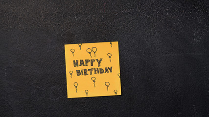 Closeup woman's hand sticking Happy Birthday note on the blackboard