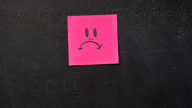 Sticky note with sad face icon on the blackboard