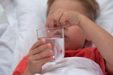 Little sick cute cboy holding a pill and a glass of water lying on the bed