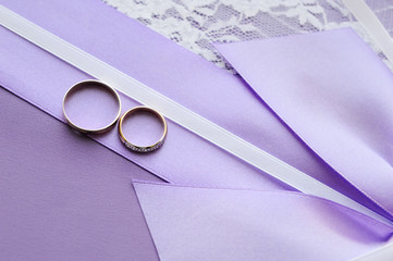 Wedding rings on a purple ribbon on a background of white fabric with lace. Geometric pattern. 