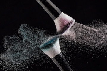 Makeup brushes with red and green powder explode on a black background