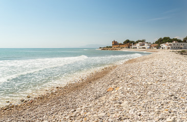 Vista de una playa de cantos rodados con un castillo pirata al fondo.