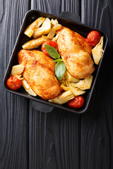 Fried chicken breasts are served with artichokes and tomatoes close-up on a plate. Vertical top view