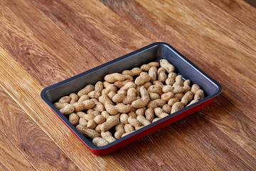 Unpeeled raw peanut on baking tray over wooden background, selective focus, shallow depth of field.