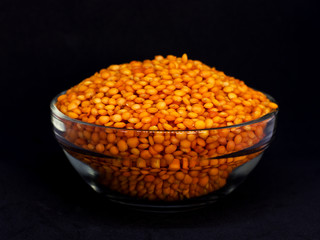 Red raw lentils in a glass bowl. Isolated on black background