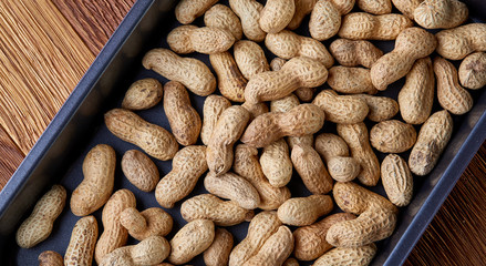 Unpeeled raw peanut on baking tray over wooden background, selective focus, shallow depth of field.