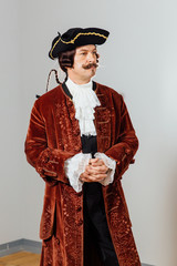 mustachioed eccentric man in the vintage clothes of the baron. Hat tricorn, brown jacket.