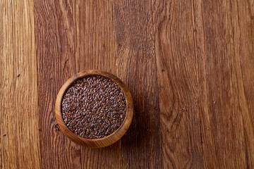 Flax seeds in a plate on wooden background, top view, close-up.