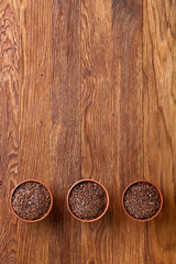 Three ceramic bowls with flaxseeds arrenged in row over wooden background, top view, selective focus