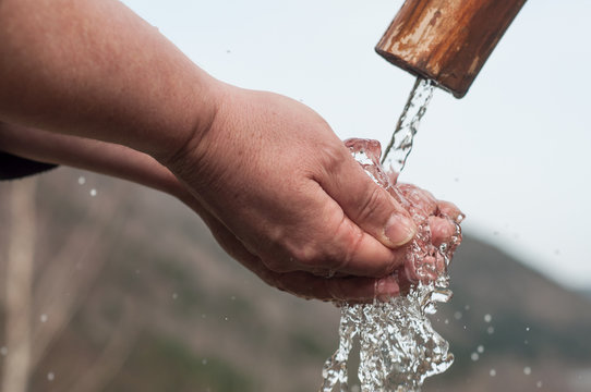 closeup of hands in the water of typical wooden fountain on moutain landscape background